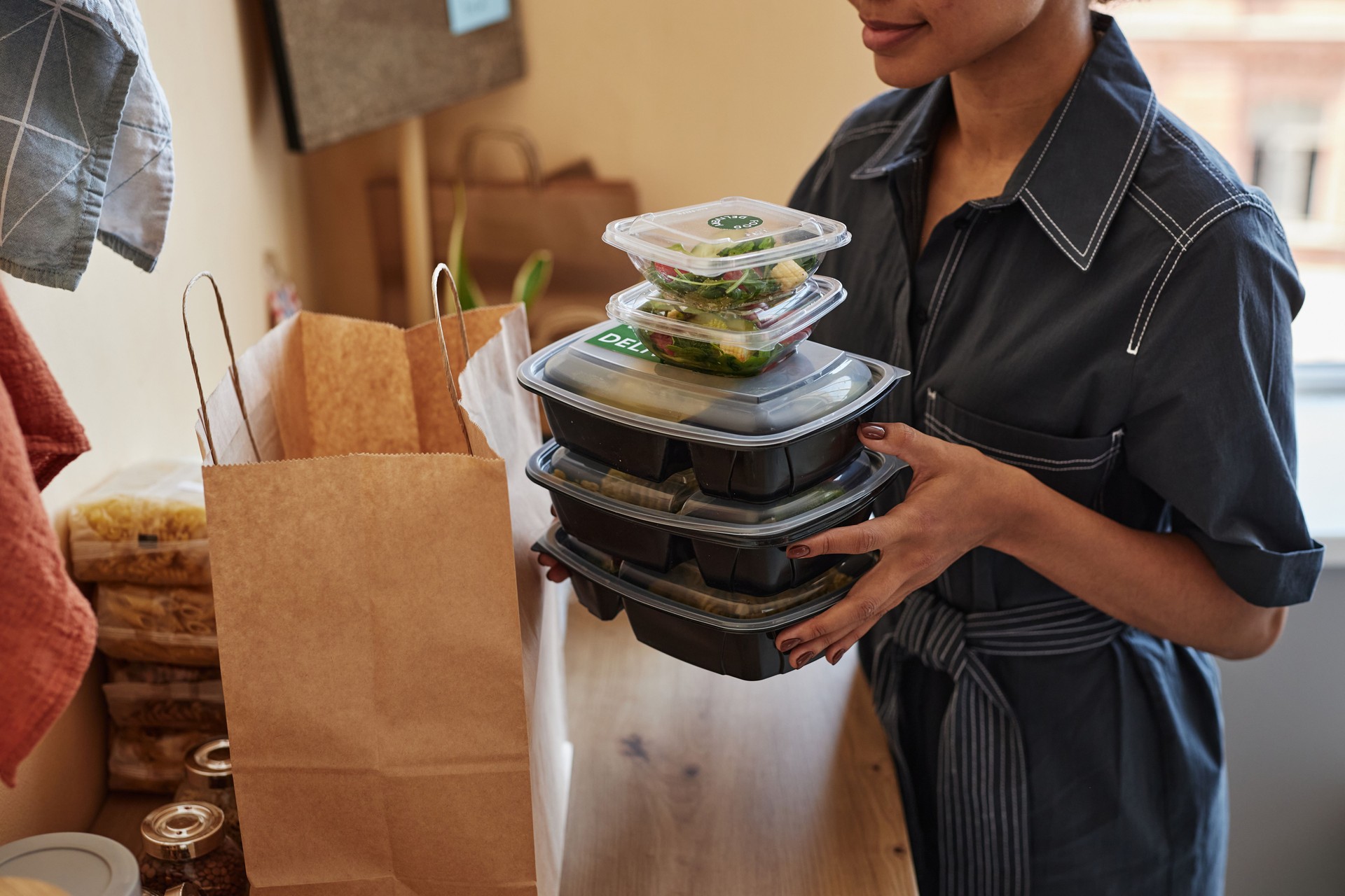 Young woman unpacking food delivery order at home kitchen
